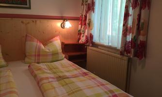 A cozy bedroom with two beds and colorful bed covers. The window is decorated with floral curtains and there is a wall lamp.
