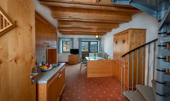 A cozy living space with wooden furniture and a spiral staircase. Large windows provide plenty of daylight and a friendly atmosphere.