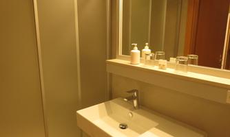 A modern bathroom with a white sink and a mirror. On the sink are care products and glasses.