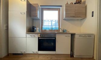 A modern kitchen with white and wooden cabinets. The stove and dishwasher are visible, and daylight comes through the window.