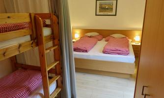 A cozy bedroom with a bunk bed and a double bed. The bed linen is checked and the room has warm lighting.