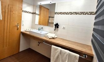 A modern bathroom with a wooden vanity and a large mirror. The walls are tiled in light colors, and fresh towels are hanging.