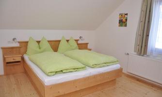 A cozy bedroom with a double bed and green bedspreads. The walls are bright, and the room is flooded with light.