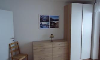 A simple room with a wooden wardrobe and a chest of drawers. A picture with nature motifs hangs on the wall.