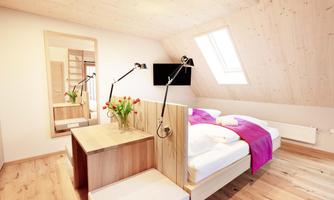 A stylish bedroom with wooden flooring and a large window. There is a modern bed, a desk, and fresh flowers on the table.