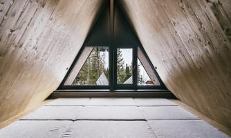 A cozy room in the attic with visible wood. Large windows offer a view of the surrounding nature.