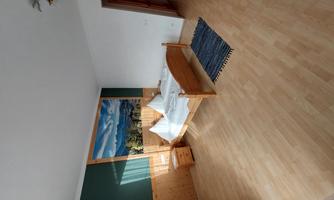 A bright bedroom with a large bed and white pillows. On the wall, there is a landscape painting featuring mountains.