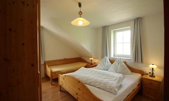 A cozy bedroom with wooden interiors. It contains a double bed, a couch, and a window with natural light.