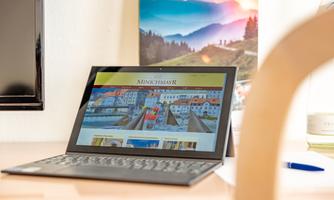 A laptop is on a table and displaying a webpage. In the background, there are pictures of landscapes and a bottle.