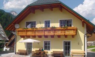 A charming yellow house with a lovingly designed balcony and a terrace. The surroundings are green and mountainous, perfect for a relaxing stay.