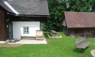 A traditional country house with a small garden. In the background, other buildings and wooden seating can be seen.