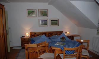 A cozy room with wooden furniture and blue bedding. Pictures of landscapes hang on the wall, and there is a small table with chairs.