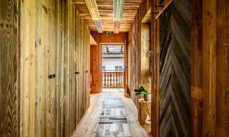 A brightly lit hallway with wooden walls and an elegant flooring. At the end of the hallway, doors and a balcony are visible.