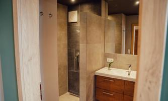A modern bathroom with a shower and a wooden sink. The walls are designed in neutral tones and there is good lighting.