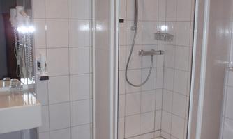 A modern bathroom with a shower and gray tiles. Next to the shower is a sink and a trash can.
