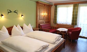 A cozy room with two beds, wooden paneling, and a small living area. Large windows let in plenty of light and provide a pleasant atmosphere.