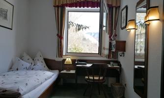 A cozy bedroom with a single bed and a desk. The window offers a view of nature.