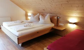 A cozy bedroom with a double bed and a separate bed. The walls are made of wood, and the lighting creates a pleasant atmosphere.