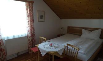 A cozy bedroom with a double bed and wooden ceiling. There is a small table with chairs and plenty of daylight through the window.