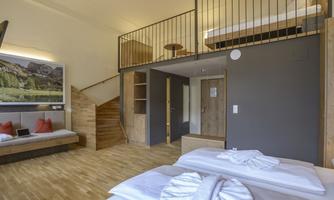 A modern room with hardwood floors and a loft-style sleeping area. The furnishings are bright and inviting, with a sofa bed and decorative cushions.
