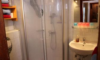A small bathroom with a shower and a sink. Towels are neatly stacked on a shelf.