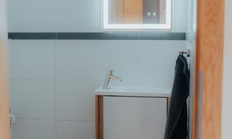 A modern bathroom with a sink and a illuminated mirror. The walls are brightly tiled, and there is a towel holder.