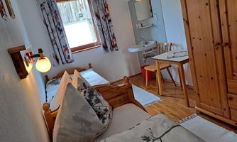 A cozy room with two beds and wooden furniture. There is a small table, a chair, and a sink.