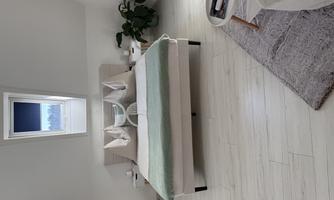 A modern bedroom with a large bed, cozy pillows, and a green throw. A plant and a small table complete the room.