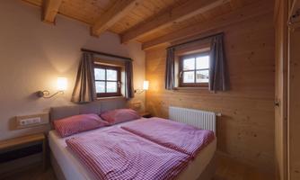 A cozy bedroom with wood paneling and two beds. Next to the windows, there are soft curtains and gentle lighting.