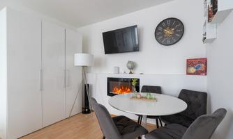 A modern living room with a round table and stylish chairs. On the wall, there is a television and an electric fireplace.