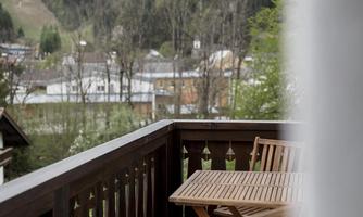 A quiet balcony with two wooden chairs and a view of a green, forested landscape. In the background, houses and hills are visible.