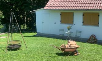 A small garden with a shed and freshly mowed grass. In the foreground is a wheelbarrow and a grill.