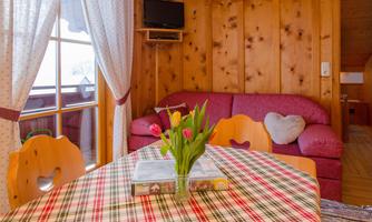 A cozy living room with wooden walls and a red sofa. On the table, there is a vase with fresh tulips and a book.