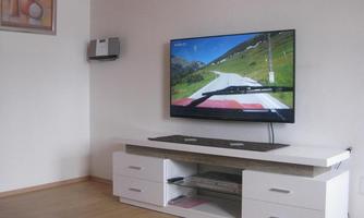 A living room with a modern TV displaying a landscape on the screen. Below it is a white TV unit with storage compartments.