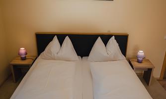 A cozy bedroom with a double bed and two nightstands. On the wall hangs a picture of a mountain landscape.