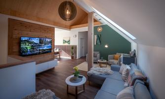 A modern living room setup with a cozy sofa and a television on the wall. The room has a bright, inviting atmosphere with wooden elements and beautiful lighting.