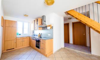 A bright kitchen with wood cabinets and modern appliances. The room has large windows and offers a view of the staircase.