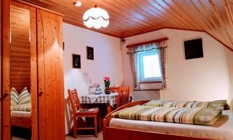 A cozy room with wooden ceilings and a sleeping area. There is a table with chairs and some decorative elements on the wall.