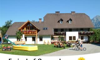 A holiday farm with a charming building and a large garden. Children are playing outside, and there are play facilities.