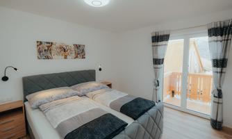 A cozy bedroom with a double bed and light walls. Large windows let in plenty of light and offer a view outside.
