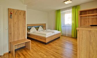 A modern room with a double bed and wooden floor. Green curtains let in plenty of light and create an inviting atmosphere.