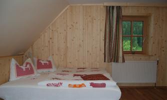 A cozy bedroom with wooden paneling and a double bed. The room features a window with a view of greenery and is simply but invitingly furnished.