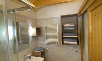 A modern bathroom with a wooden ceiling and large tiles. It features a sink, a shower, and a towel radiator.