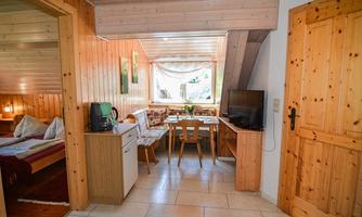 A cozy room with wood paneling, a table, and chairs. The room has windows overlooking the outdoors and a kitchenette.