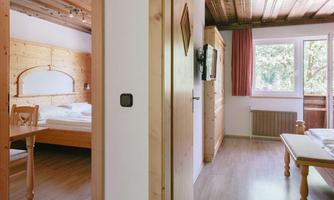 A bright and cozy room with wooden decor. There is a bed, a table, and large windows that let in light.