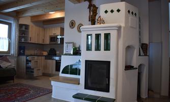A cozy living room with a modern wood stove and an open kitchen. The walls are light, and there are decorative elements that give the room character.