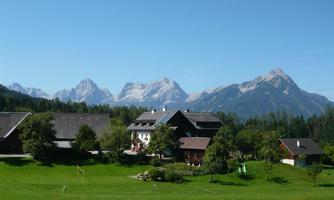 An idyllic landscape with typical mountain houses and green meadows. In the background, majestic mountains rise under a clear blue sky.
