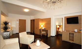 A modern room with a cozy seating area and warm colors. A television stands next to a desk, and the room features stylish lighting.