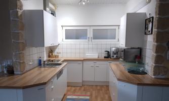 A modern kitchen with wooden countertops and white cabinets. The large window front provides plenty of daylight.