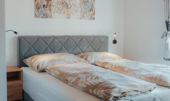 A modern bedroom with two single beds and a gray bed frame. The walls are painted light, and a decorative picture hangs above the bed.